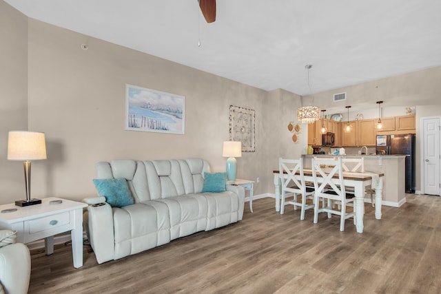 living area with light wood finished floors, visible vents, baseboards, and ceiling fan with notable chandelier