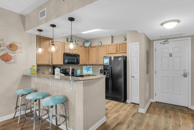 kitchen featuring a peninsula, light stone countertops, backsplash, and black appliances