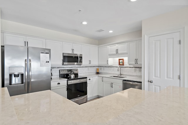 kitchen featuring stainless steel appliances, a sink, light stone counters, white cabinetry, and recessed lighting