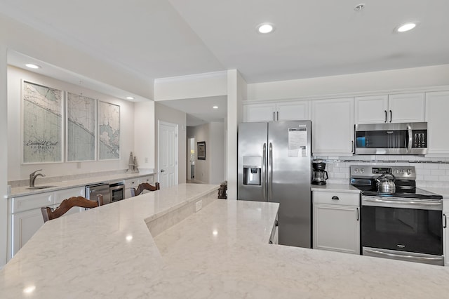 kitchen featuring appliances with stainless steel finishes, a sink, light stone counters, white cabinetry, and backsplash
