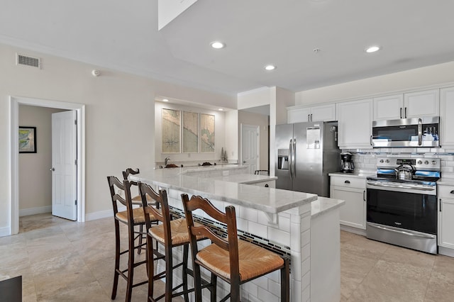 kitchen with appliances with stainless steel finishes, a kitchen breakfast bar, white cabinets, light stone countertops, and decorative backsplash