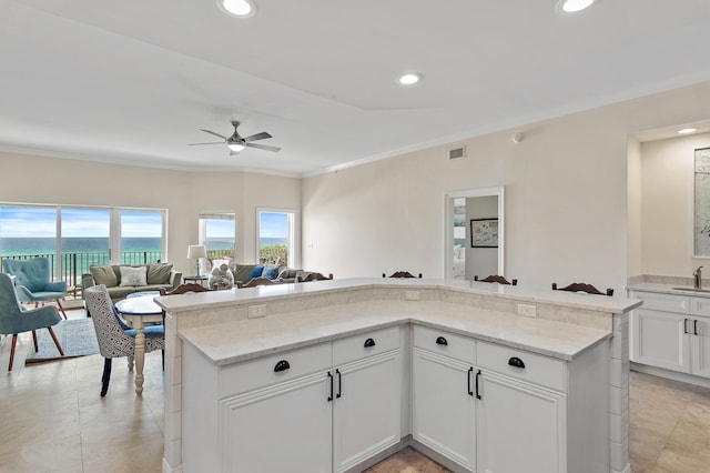 kitchen featuring a sink, a ceiling fan, ornamental molding, open floor plan, and light stone countertops