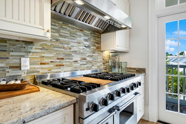 kitchen featuring backsplash, range with two ovens, light stone countertops, premium range hood, and white cabinetry