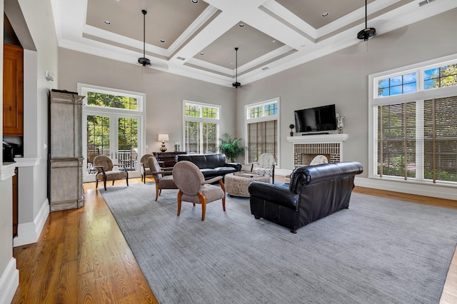 living room featuring a ceiling fan, a towering ceiling, a fireplace, light wood-type flooring, and ornamental molding