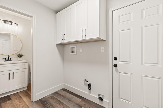 clothes washing area featuring wood finished floors, baseboards, hookup for a washing machine, a sink, and cabinet space