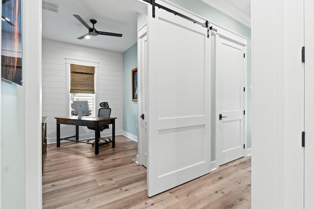 hallway featuring visible vents, a barn door, light wood-style flooring, and baseboards