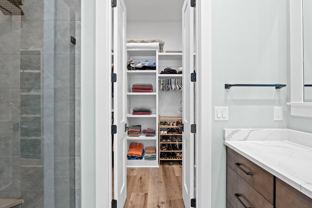 bathroom featuring vanity, a stall shower, a walk in closet, and wood finished floors