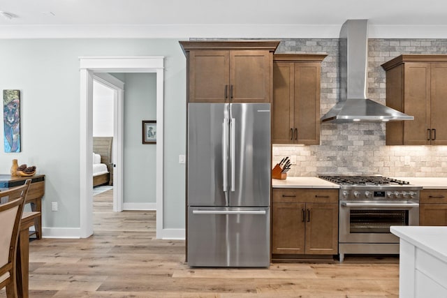 kitchen with wall chimney range hood, backsplash, light countertops, stainless steel appliances, and light wood-style flooring