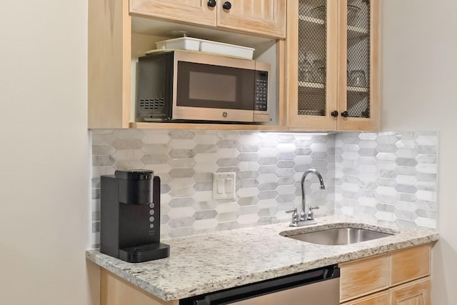 kitchen with backsplash, appliances with stainless steel finishes, light brown cabinetry, a sink, and glass insert cabinets