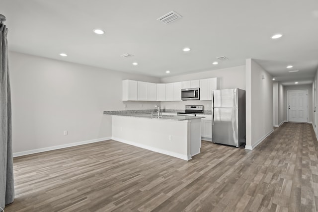 kitchen with a peninsula, wood finished floors, visible vents, white cabinets, and appliances with stainless steel finishes
