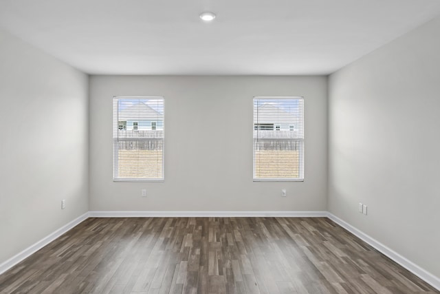 empty room with a wealth of natural light, baseboards, and dark wood-type flooring