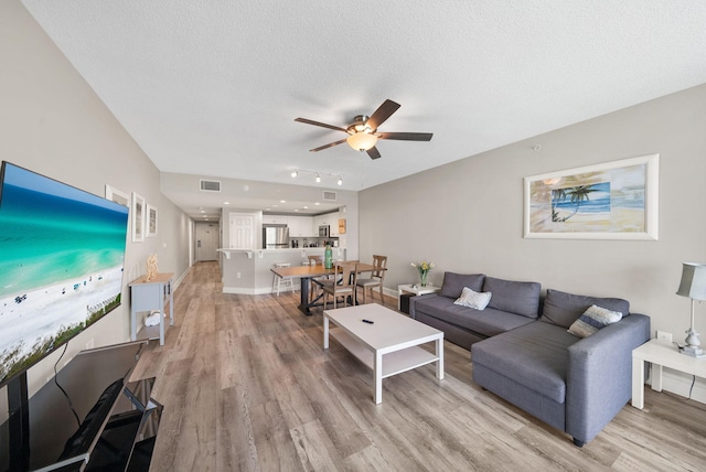 living room with a ceiling fan, light wood-type flooring, a textured ceiling, and visible vents