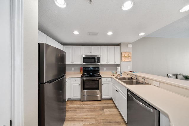kitchen featuring appliances with stainless steel finishes, a sink, light countertops, light wood-style floors, and white cabinetry