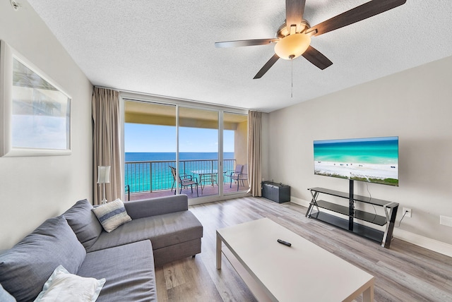 living area featuring ceiling fan, a wall of windows, a textured ceiling, baseboards, and wood finished floors