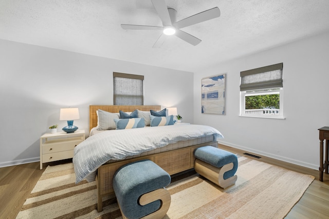 bedroom featuring ceiling fan, light wood-style floors, a textured ceiling, baseboards, and visible vents