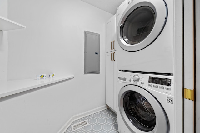 laundry area with visible vents, stacked washer / dryer, baseboards, electric panel, and cabinet space