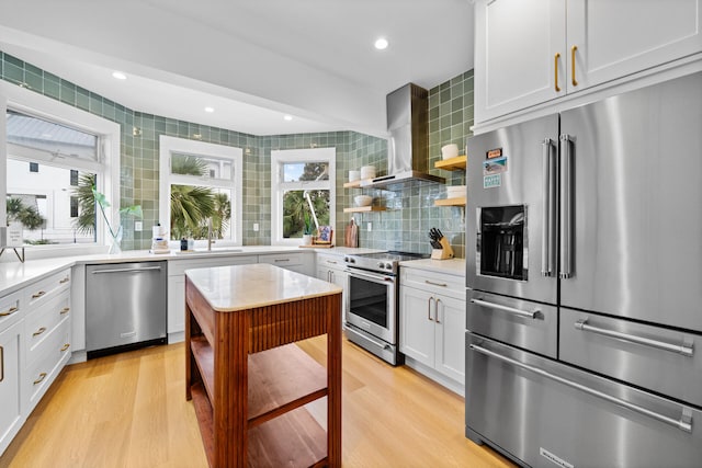 kitchen with wall chimney range hood, open shelves, a sink, backsplash, and premium appliances