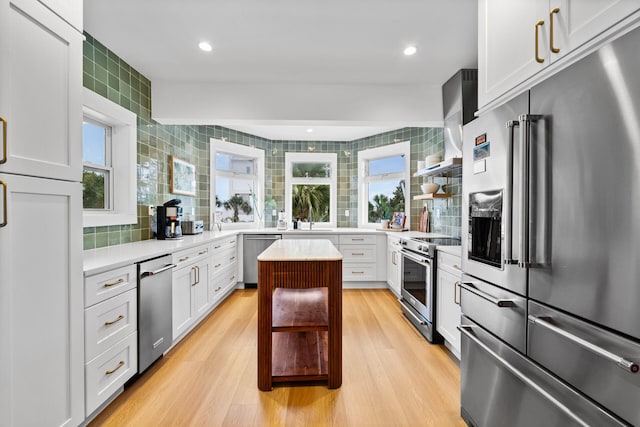 kitchen with wall chimney range hood, light countertops, backsplash, and high quality appliances