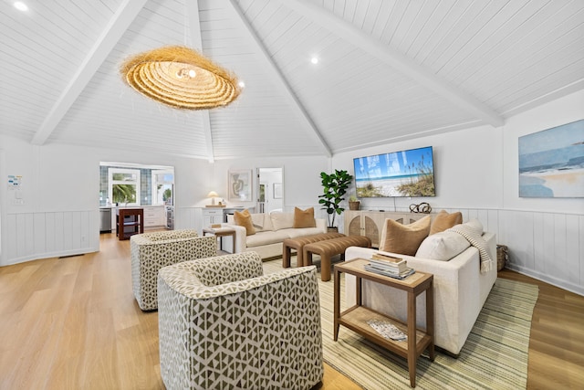 living area featuring lofted ceiling with beams, light wood-style flooring, and wainscoting