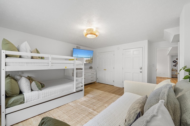 bedroom with a textured ceiling, multiple closets, and light wood finished floors