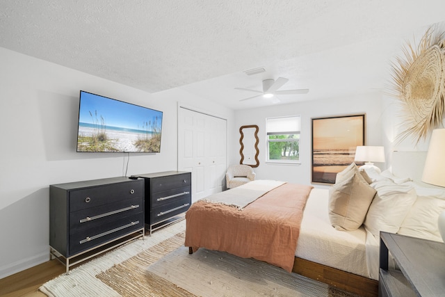 bedroom featuring a ceiling fan, a textured ceiling, baseboards, a closet, and light wood-style floors