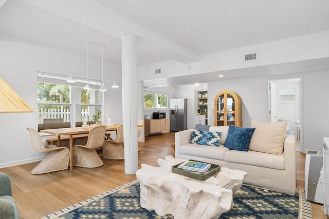 living room featuring light wood-style floors, visible vents, and beamed ceiling