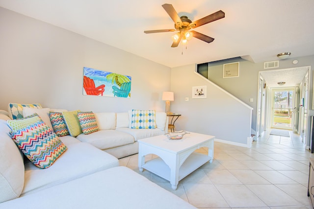 living area with light tile patterned floors, a ceiling fan, visible vents, baseboards, and stairway