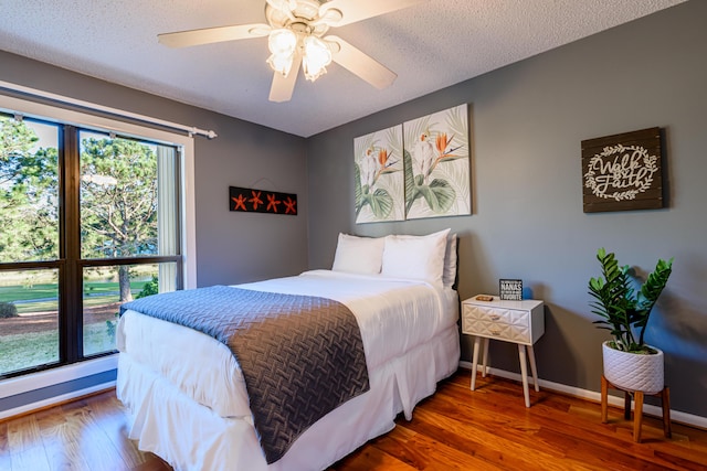 bedroom featuring ceiling fan, a textured ceiling, baseboards, and wood finished floors