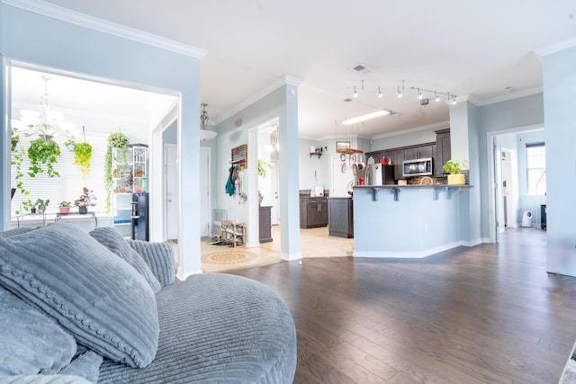 living area featuring an inviting chandelier, baseboards, wood finished floors, visible vents, and ornamental molding