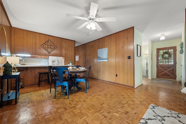 dining area featuring baseboards, a ceiling fan, and wood walls