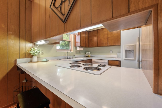 kitchen featuring brown cabinetry, a sink, light countertops, a breakfast bar, and white appliances