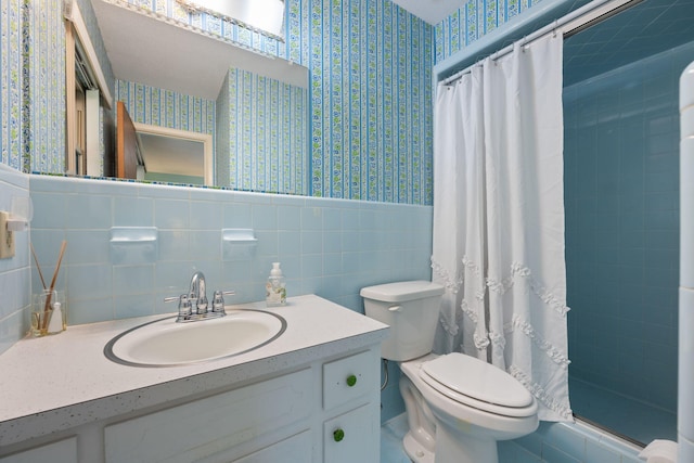 bathroom with vanity, toilet, a wainscoted wall, wallpapered walls, and a stall shower