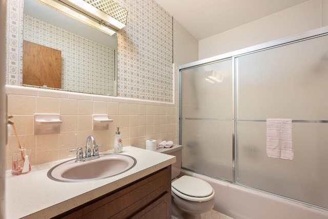 full bathroom featuring vanity, toilet, tile walls, a wainscoted wall, and combined bath / shower with glass door