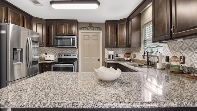 199 W Italian Ave, Defuniak Springs, FL 32433 - kitchen with appliances with stainless steel finishes, a sink, dark brown cabinets, light stone countertops, and decorative backsplash