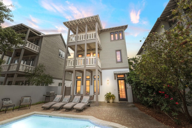rear view of property featuring fence, stucco siding, an outdoor pool, a balcony, and a patio