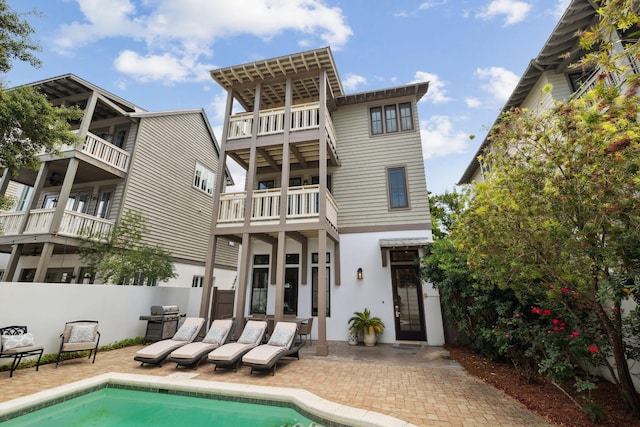 back of property featuring fence, stucco siding, an outdoor pool, a balcony, and a patio