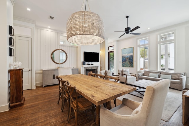 dining area featuring a warm lit fireplace, a ceiling fan, dark wood-style floors, and visible vents