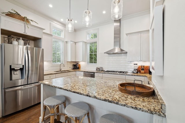 kitchen with a kitchen bar, wall chimney exhaust hood, tasteful backsplash, a sink, and appliances with stainless steel finishes