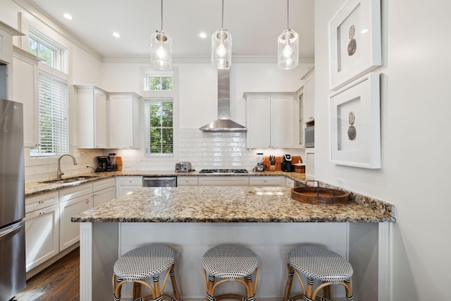 kitchen with a sink, stainless steel appliances, a kitchen bar, and wall chimney exhaust hood
