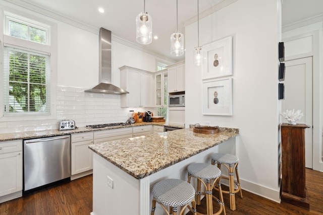 kitchen featuring dark wood-style flooring, appliances with stainless steel finishes, a breakfast bar, wall chimney exhaust hood, and tasteful backsplash