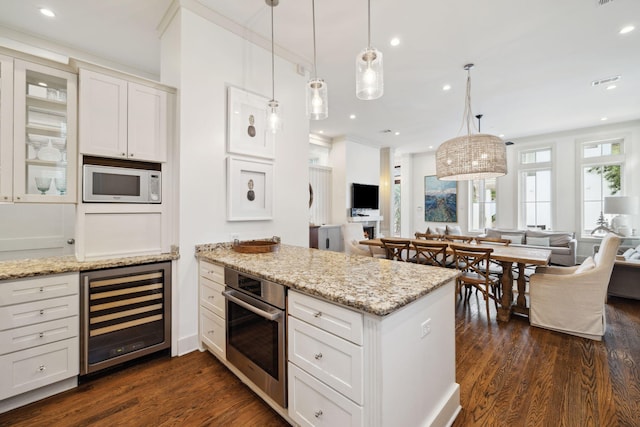 kitchen with white microwave, a peninsula, beverage cooler, open floor plan, and oven