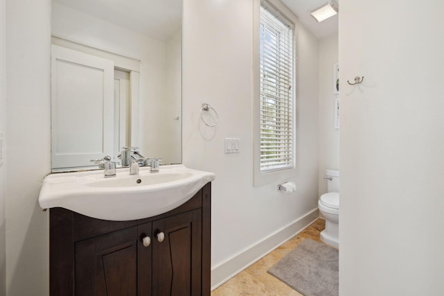 half bathroom featuring vanity, baseboards, a healthy amount of sunlight, and toilet