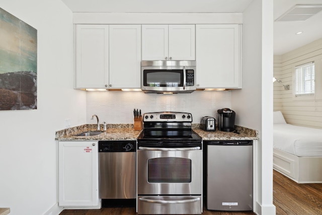 kitchen with light stone countertops, a sink, stainless steel appliances, white cabinetry, and backsplash