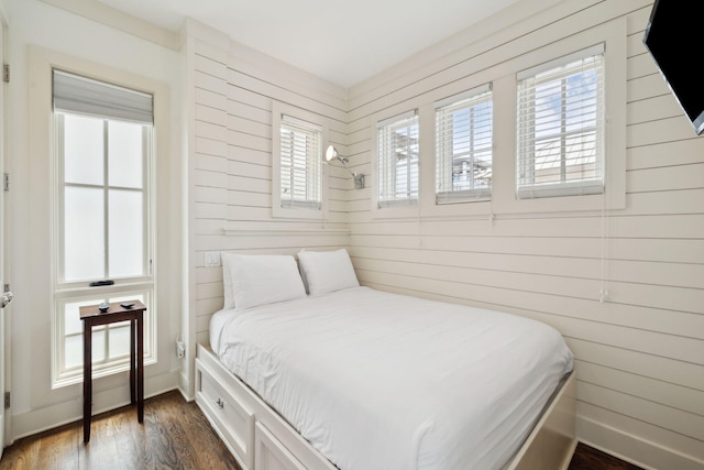 bedroom featuring dark wood-style flooring, wood walls, and multiple windows
