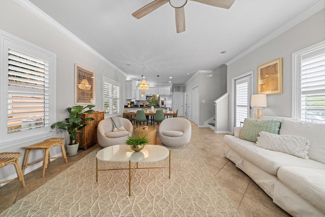 living area with light tile patterned floors, plenty of natural light, ceiling fan, ornamental molding, and baseboards