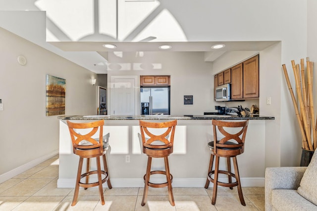 kitchen with a peninsula, appliances with stainless steel finishes, brown cabinetry, and a kitchen breakfast bar