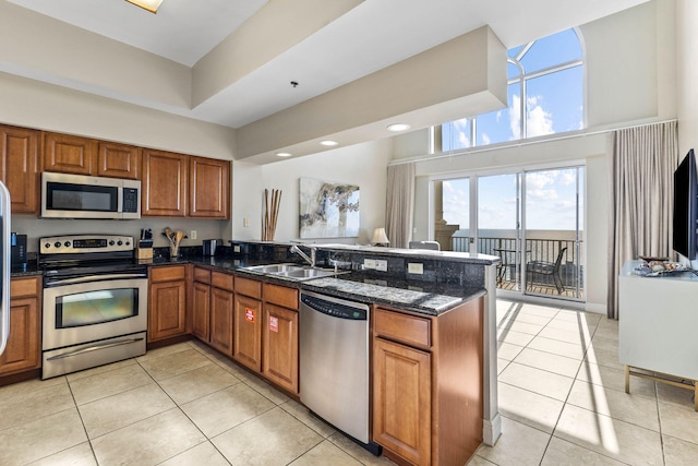 kitchen with a peninsula, brown cabinets, a towering ceiling, light tile patterned floors, and appliances with stainless steel finishes