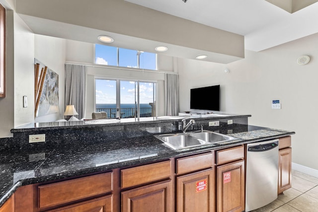 kitchen featuring brown cabinets, a sink, open floor plan, stainless steel dishwasher, and light tile patterned flooring