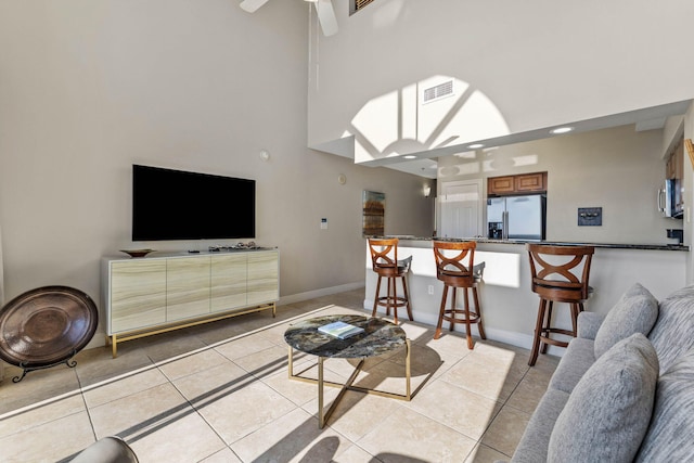 living room with light tile patterned floors, a ceiling fan, a high ceiling, visible vents, and baseboards