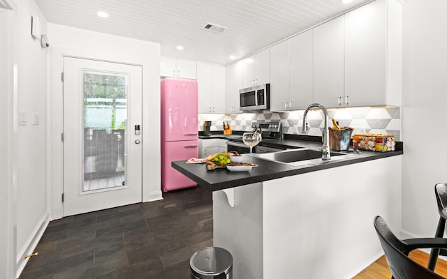 kitchen featuring a peninsula, a sink, dark countertops, stainless steel appliances, and visible vents